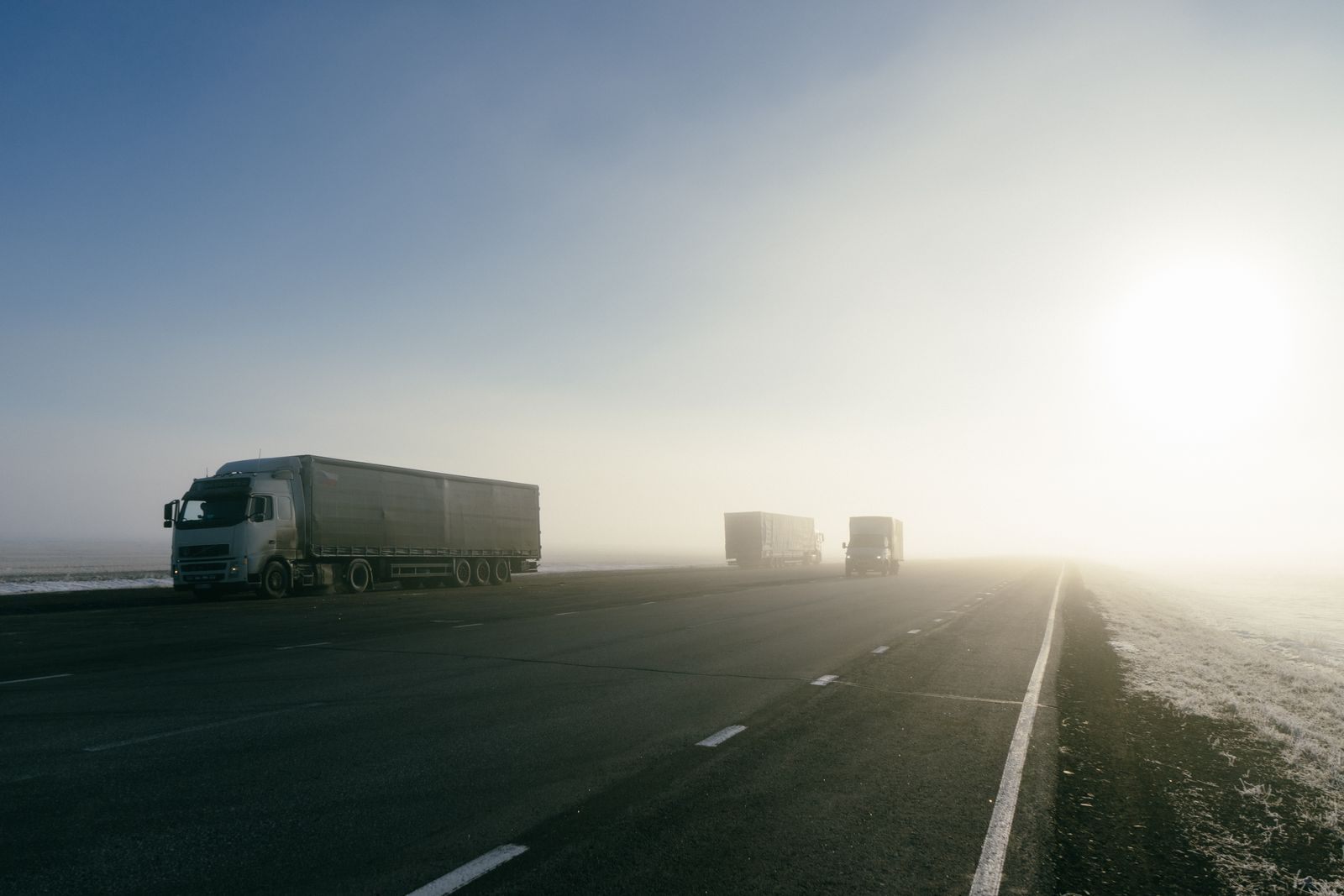 Freight trucks on a foggy road during sunrise, showcasing transportation in misty conditions